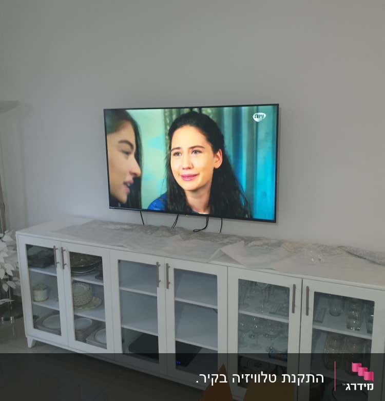 טלוויזיה מותקנת על קיר מעל ארונית לבנה